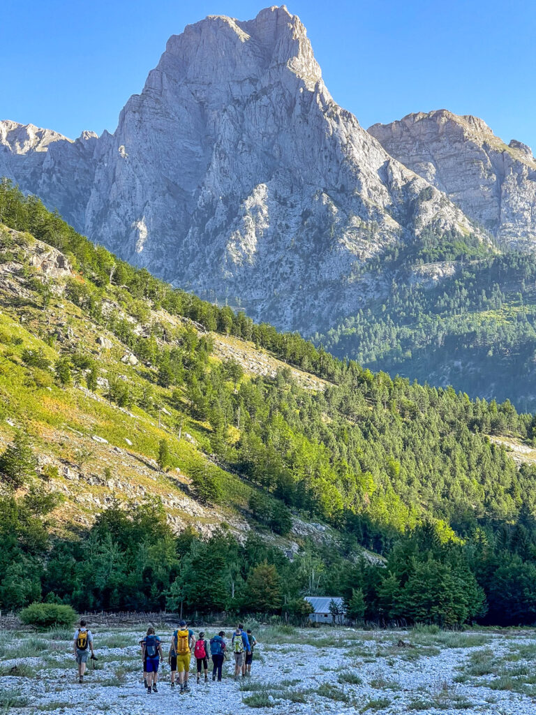 Eine kleine Gruppe auf Wanderreise im Balkan geht über eine steinige Ebene auf einen hohen, kahlen Berg im Hintergrund zu.