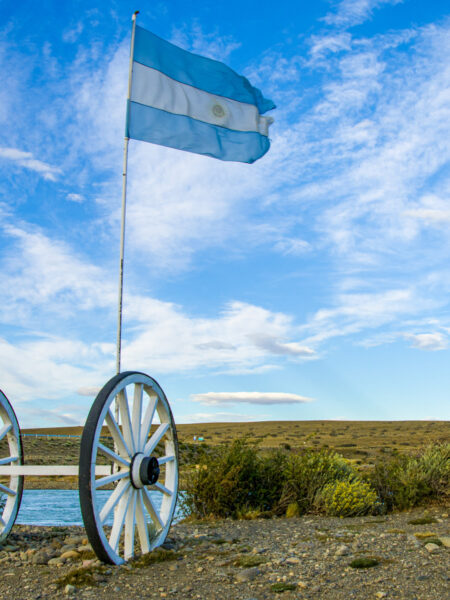 Die argentinische Flagge weht im Wind über einen kleinen Wagen, der am Wegesrand eines Wanderpfades abgestellt wurde.