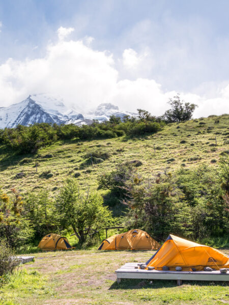 Mehrere Zelte stehen auf einem Platz an einem Hang in Patagonien. Sie dienen den Wanderreisenden von Weltweitwandern als Schlafstätte während ihrem Trekk im Torres del Plaine.