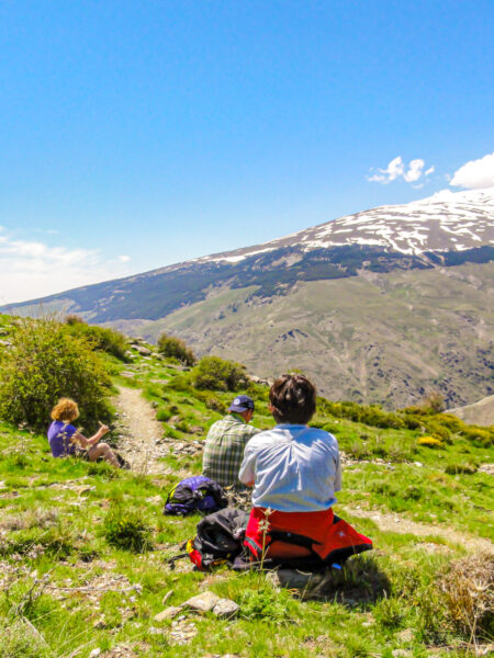 Drei Personen sitzen am Wegesrand neben einem Wanderweg auf ihrer Trekkingtour durch die Gebirgsregion Alpujarras.