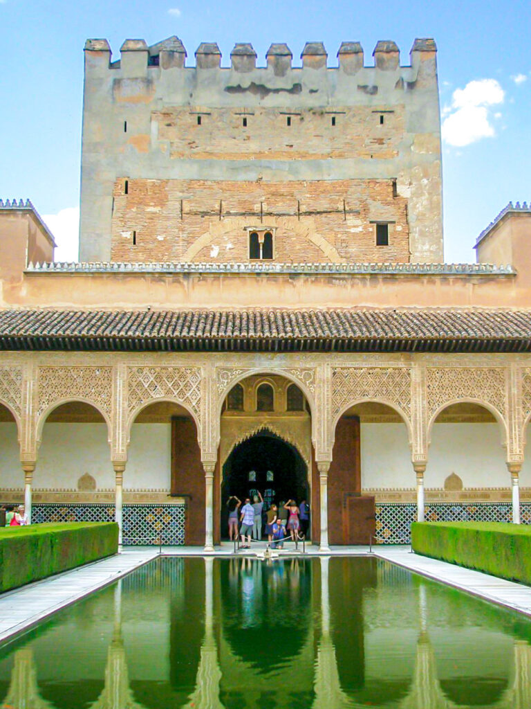 Ein Fot des Patio de la Acequia (Hof des Wasserkanals) in den Gärten des Generalife, einem Teil der Alhambra in Granada. Vor dem Tor stehen ein paar Personen auf Wanderreise.