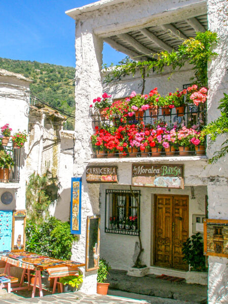Der Eingang einer kleinen Taverne in einer Ortschaft im Süden von Spanien in der Region Andalusien. Am Balkon über dem Eingang wachsen einige Blumen.