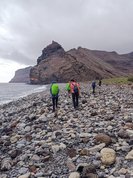 Vier Personen auf einer Wanderreise mit Weltweitwandern gehen einen felsigen Strand auf der Insel La Gomera entlang.