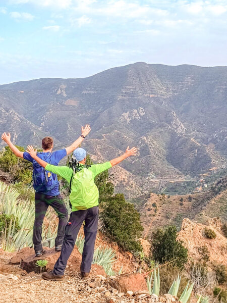 Zwei Personen mit Wanderrucksäcken stehen vor eine beeindruckenden Aussicht auf La Gomera. Beide haben die Arme ausgestreckt und jubeln ins Tal auf der kanarischen Insel hinunter.