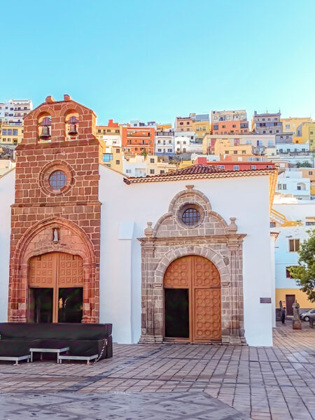 Das Bild zeigt die Kirche Nuestra Señora de la Asunción (Kirche Mariä Himmelfahrt) in San Sebastián de La Gomera. Im Hintergrund erhebet sich die kanarische Küstenstadt auf dem Hügel.