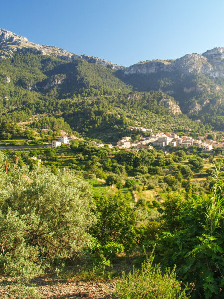 Man sieht Teile des Serra de Tramunta auf Mallorca. Das Foto zeigt eine kleine Ortschaft im Gebirge, sowie Teile der Gebirgskette im Hintergrund.