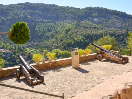Zwei historische Kanonen stehen auf der Stadtmauer von Deia in Mallorca und zielen hinab in das Tal darunter.