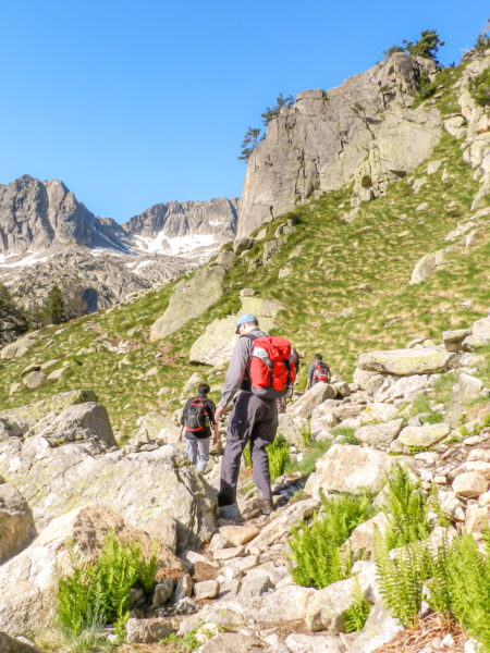Zwei Personen auf einer Wanderreise folgen einem felsigen Pfad durch die Pyrenäen im Norden von Spanien. Die hinter Person trägt einen roten Rucksack von Weltweitwandern.
