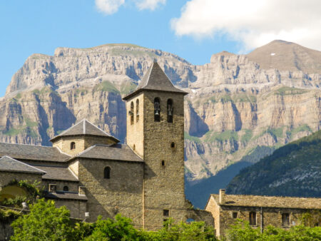 Die Kirche San Salvador im Dorf Torla steht vor dem beeindruckenden Massiv des Monte Perdido, einem Berg in den spanischen Pyrenäen, im Hintergrund.