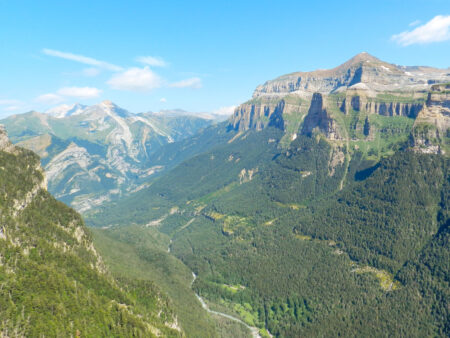 Ein Landschaftsfoto des Ordesa-Nationalparks in Nordspanien. Man sieht karge Felswände, die über saftig-grünen Wäldern in den Pyrenäen aufragen.
