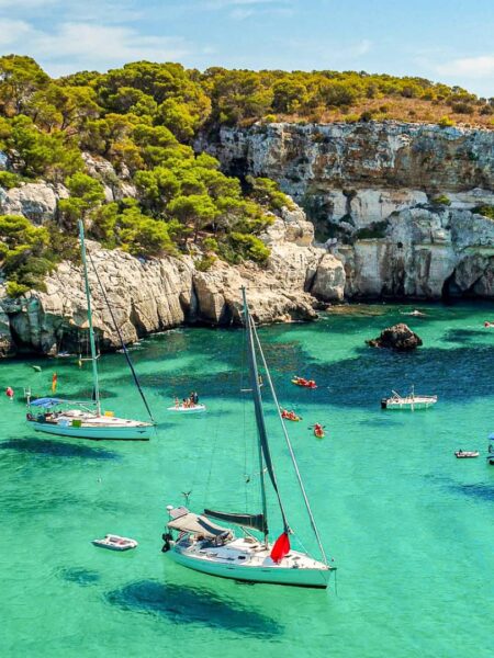 Boote treiben in der Cala Macarella an der Küste der Baleareninsel Menorca, wo kleine Reisegruppen von Weltweitwandern auf ihren Wanderungen vorbeigeführt werden.