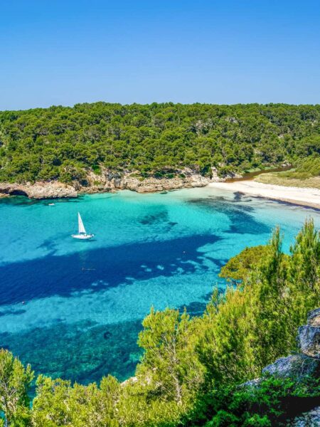 Eine strahend-blaue Bucht auf Menorca mit einem Schiff.