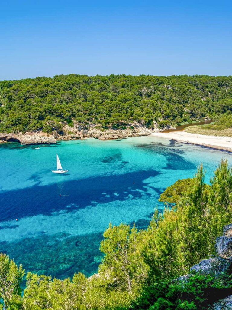 Eine strahend-blaue Bucht auf Menorca mit einem Schiff.