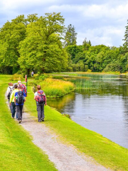 Mehrere Personen auf einer Wanderreise werden entlang eines Gewässer innerhalb der schön gepflegten Gärten von Ashford Castle.