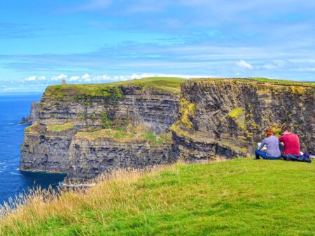 Zwei Personen sitzen an den Cliffs of Moher und schauen auf atemberaubenden Ausblick über die Klippen Irlands und den Atlantik hinaus.