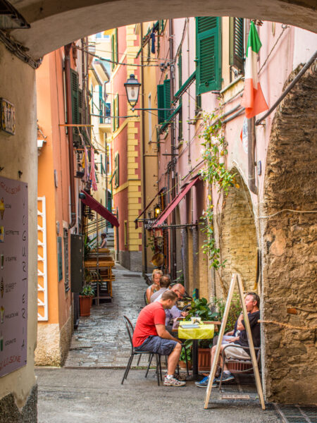 Mehrere Personen auf Wanderreise durch Ligurien sitzen in einem Café oder Restaurant in einer schmalen Gasse in der Altstadt von Monterosso.