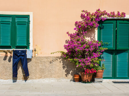 Man sieht eine gelbe Hausfassade in Riva Trigoso mit grünen Fensterläden.
