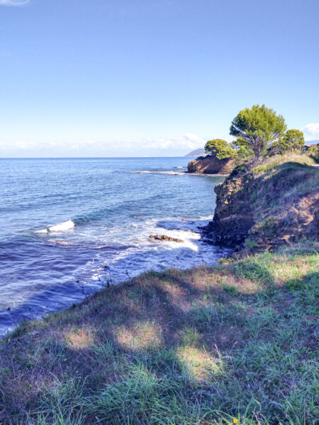 Die Küste des Cilento in Italien ist im Bild sichtbar. Man erkennt schroffe Felsen und grüne Büsche.