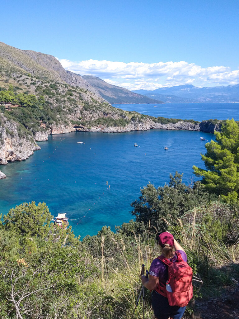 Eine Person auf Wanderreise steht an einer Bucht im Cilento und schaut auf das Meer hinaus.