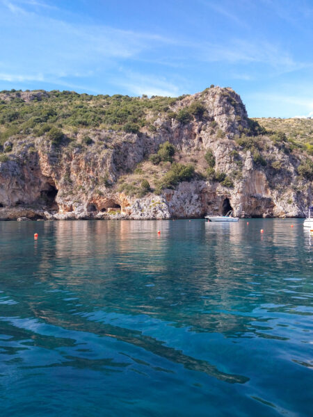 Die steilen Klippen einer Bucht im Cilento in Italien im Hintergrund des Bildes ragen über das strahlend blaue Wasser des Meeres hinaus. Das Foto ist vom Wasser aus gemacht, im Zuge eines Boots-Ausflugs bei einer Wanderreise.