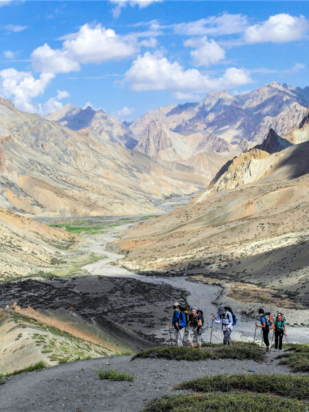 Eine Gruppe auf Wanderreise geht hinunter ins Industal. Hinter ihnen breitet sich im Bild das Tal in Ladakh aus.