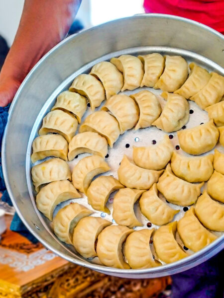 Einige Mokmoks liegen auf einem Teller aus Metall, der in die Kamera gehalten wird. Sie sind Teile des Essens, das eine Gruppe auf Wanderreise durch Ladakh bekommt.