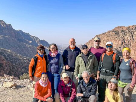 Eine Wandergruppe steht in den Bergen von Jordanien und lächelt glücklich in die Kamera. Hinter ihnen sieht man die Berge, die sie auch in ihrer Wanderreise begehen.