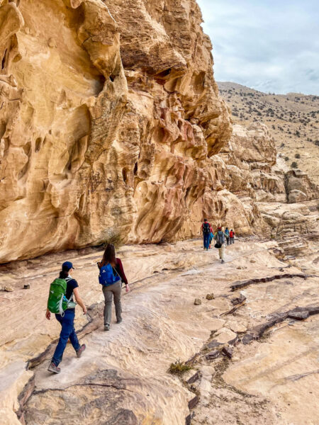 Mehrere Personen auf Wanderreise folgen einem Pfad in den Wüstenschluchten von Petra in Jordanien.