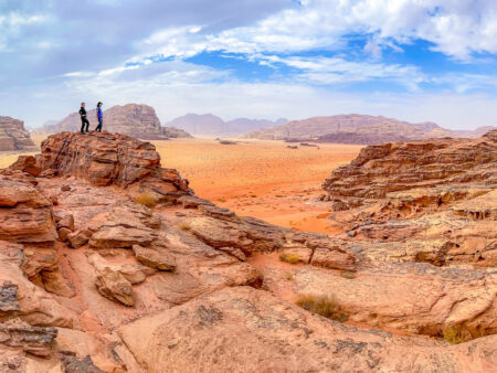 Zwei Personen auf Wanderreise steht auf einem Felsen in der jordanischen Wüste und schauen in den Horizont hinaus.