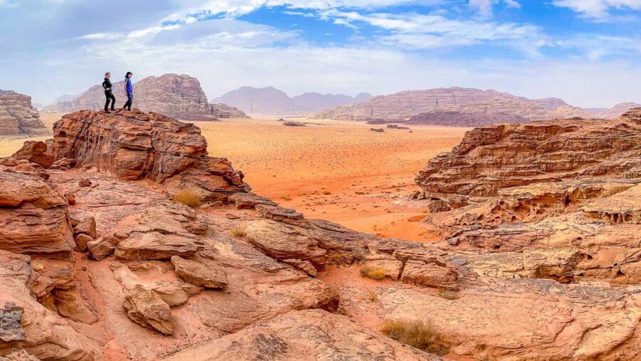 Zwei Personen auf Wanderreise steht auf einem Felsen in der jordanischen Wüste und schauen in den Horizont hinaus.