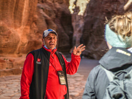 Ein Guide von Weltweitwandern steht vor einer Gruppe Reisender und erklärt ihnen interessante Informationen rund um die Felsenstadt Petra, das Ziel ihrer Reise.