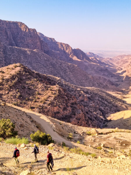 Drei Personen auf einer Wanderreise mit Weltweitwandern, folgen einem breiten Weg im Dana Naturreservat in Jordanien.