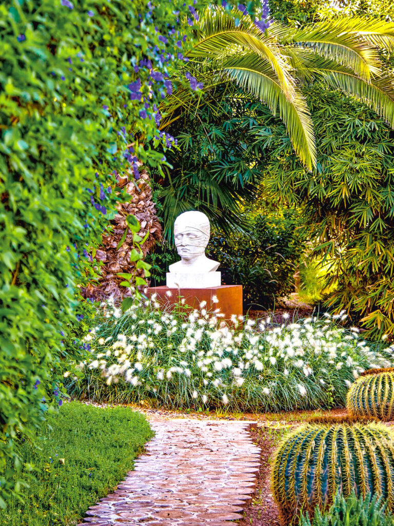 Man sieht eine Steinbüste im Anima Garden (oder Andre Heller Garten) in Marakesh. Sie ist umringt von bunter Natur kräftigen Grüntönen des Gartens.