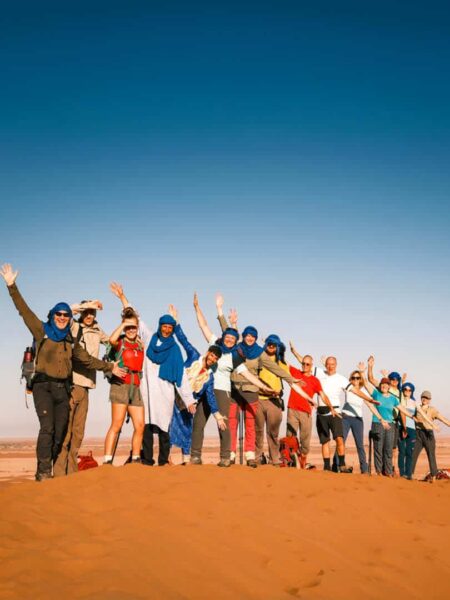 Eine Reisegruppe steht auf einer Sanddüne in der Sahara in Marokko. Sie posieren vor dem blauen Himmel der Wüste, in die sie im Zuge ihrer Wanderreise gekommen sind.