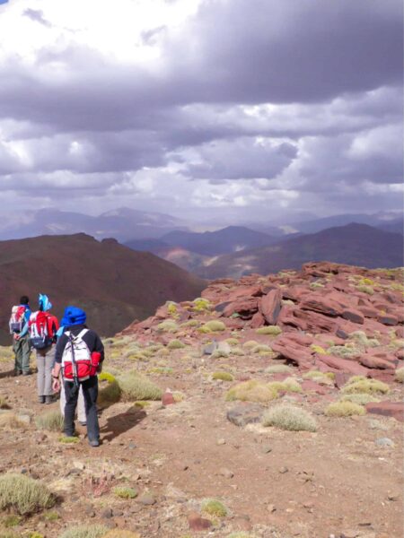 Drei Personen auf einer Wanderreise bestaunen die Aussicht auf den Hohen Atlas in Marokko. Sie befginden sich an einem hohen Punkt im Gebirge, den sie gerade auf ihrer Trekkingreise erklommen haben.