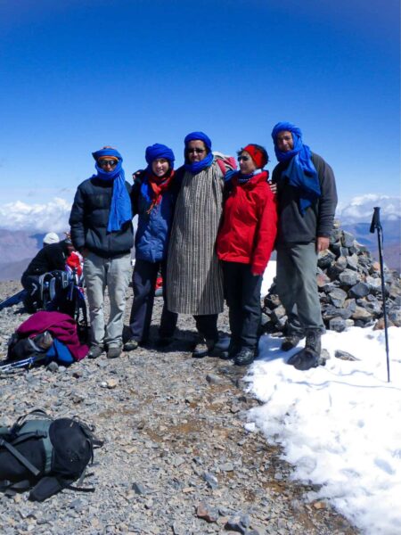Ein Gruppenfoto von Wanderreisenden in Marokko vom Gipfel des M'Goun aus. Hinter ihnen kann man Teile der Landschaft des Hohen Atlas in Marokko sehen.