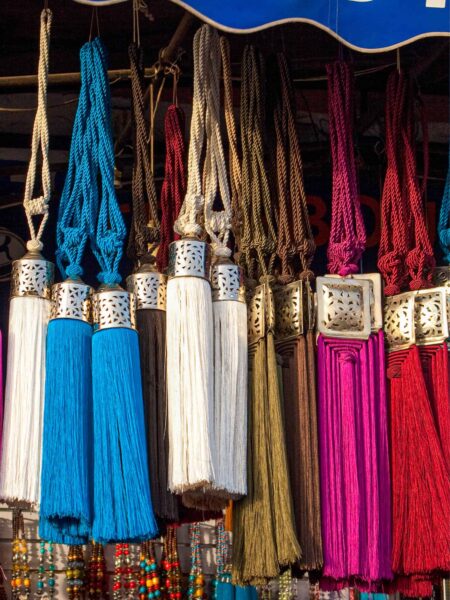 Man sieht farbenprächtige Kordeln in einem Geschäftslokal in Marrakesch. Es handelt sich dabei um marokkanische Quasten und Raffhalter mit eingravierten Silberkugeln.