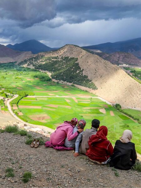 Eine kleine Gruppe aus Wanderreisenden sitzt an einem Hang im Hohen Atlas in Marokko und schaut hinunter auf das Grüne Aït Bougoumez-Tal.