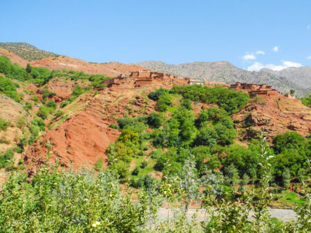 Ein Panoramabild aus dem Toubkal-Nationalpark in Marokko, das durch das Farbenspiel von rotem Sandstein und grünen Büschen und Bäumchen besticht.