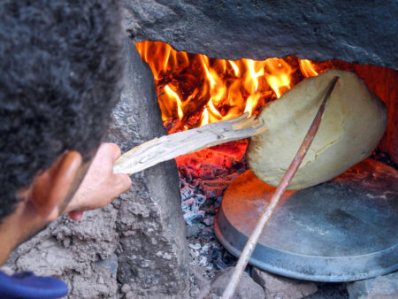 Ein Guide von Weltweitwandern backt traditionelles Fladenbrot in einer kleinen Steinhöhle. In dem improvisierten Ofen lodern die Flammen, die er nutzt, um das Brot zu garen.