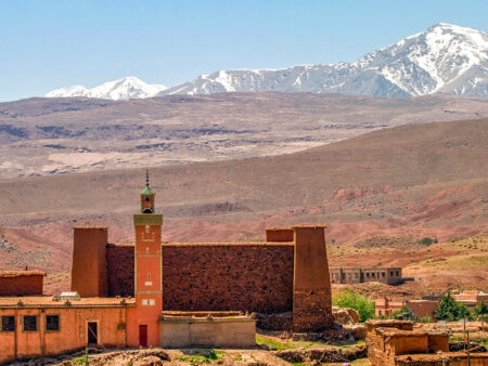 Man sieht eine Siedlung im Hohen Atlas inklusive des Turms einer Moschee. Im Hintergrund erheben sich die Gipfel des nordafrikanischen Gebirges.