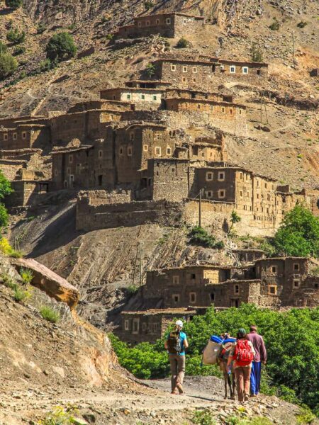 Ein kleine Wandergruppe mit einem Esel geht auf ein Bergdorf im Hohen Atlas in Marokko zu.