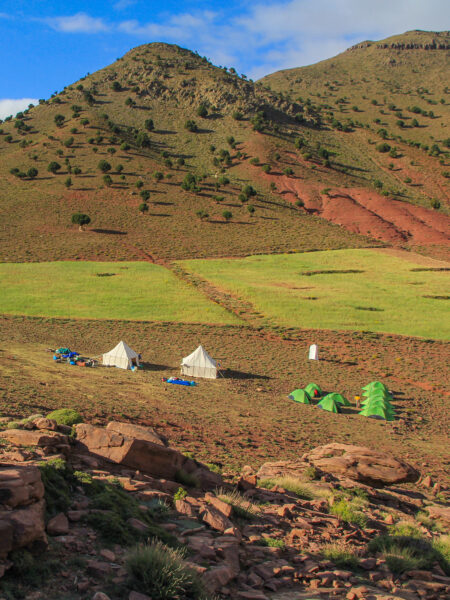 Ein kleines Zeltlager einer Reisegruppe von Weltweitwandern steht vor dem Hintergrund der Berge des Hohen Atlas in Marokko.