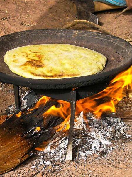 Ein Fladenbrot liegt in einer Pfanne über einem Lagerfeuer einer Reisegruppe von Weltweitwandern in Marokko. Das Feuer brennt in einem der Camps, das die Gruppe auf ihrer Reise durch den Hohen Atlas aufgeschlagen hat.