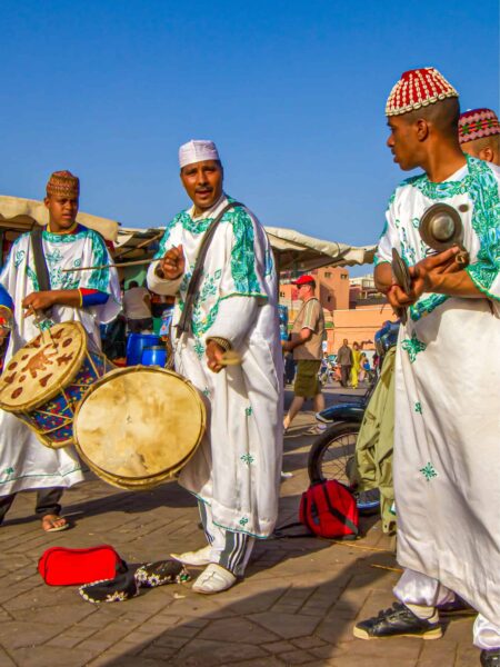 Drei Straßenmusiker spielen etwas auf Trommeln und anderen Instrumenten auf den Straßen von Marrakesch.