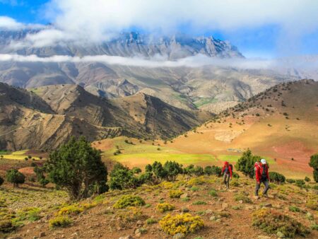 Zwei Mitglieder einer kleinen Reisegruppe von Weltweitwandern, erklimmen einen Anhöhe im Hohen Atlas in Marokko. Hinter ihnen sieht man die Berglandschaft in Nordafrika, die sie auf ihrer Trekkingreise mit Weltweitwandern bereits durchquert haben.