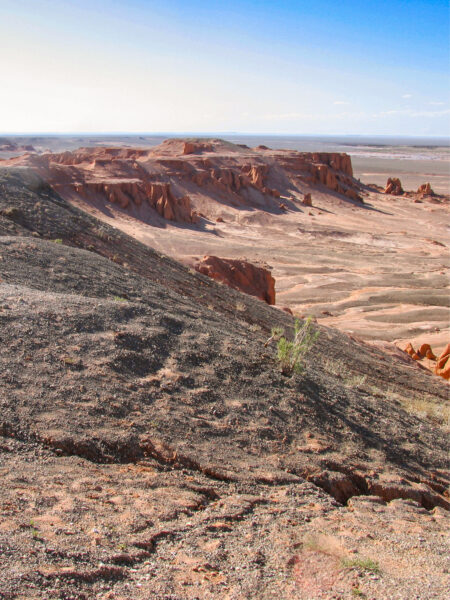 Auf dem Bild kann man die Flaming Cliffs in der Wüste Gobi in der Mongolei sehen. Der rote Fels hebt sich von der kargen restlichen Landschaft ab.