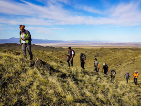 Mehrere Reisende auf einer Trekkingreise durch die Mongolei folgen ihrem Local Guide durch die hügelige Steppenlandschaft in Zentralasien.