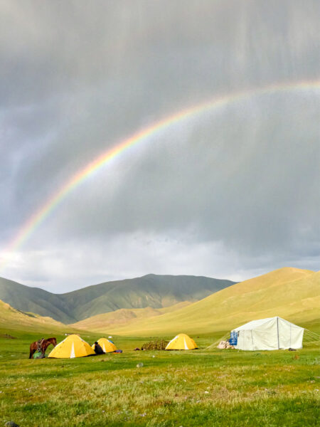 Man sieht das Camp einer Trekkinggruppe in der Mongolei aus ein bisschen Distanz. Im Hintergrund ging gerade ein Sturm herunter und ein Regenbogen überspannt das Camp.