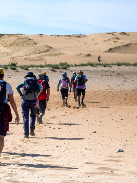 Eine kleine Gruppe wandert am Rande der Wüste Gobi durch den Sand. Sie sind am Weg zu ihrem Camp im Westen der Mongolei.